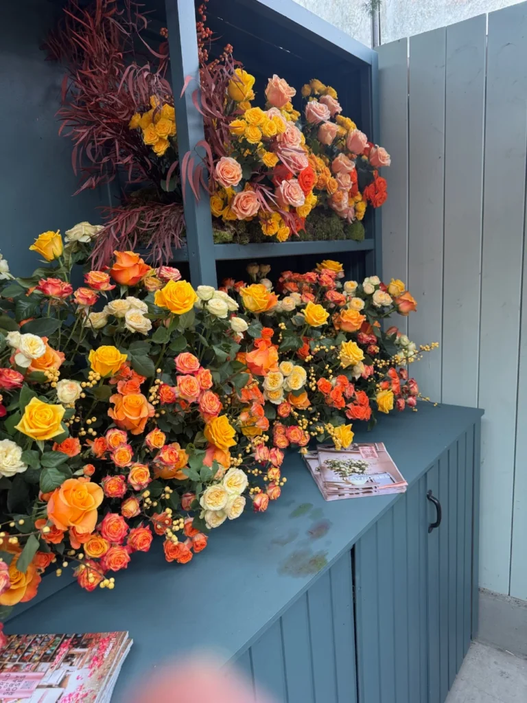 Large-scale floral wall installation featuring orange, yellow, and pink roses at Dutch flower trade show venue