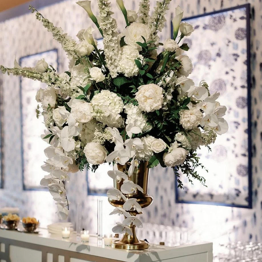 Large white wedding flower arrangement featuring hydrangea, peonies, roses, orchids, and delphinium in a gold urn, inspired by Cloud Dancer Pantone Color of the Year 2026