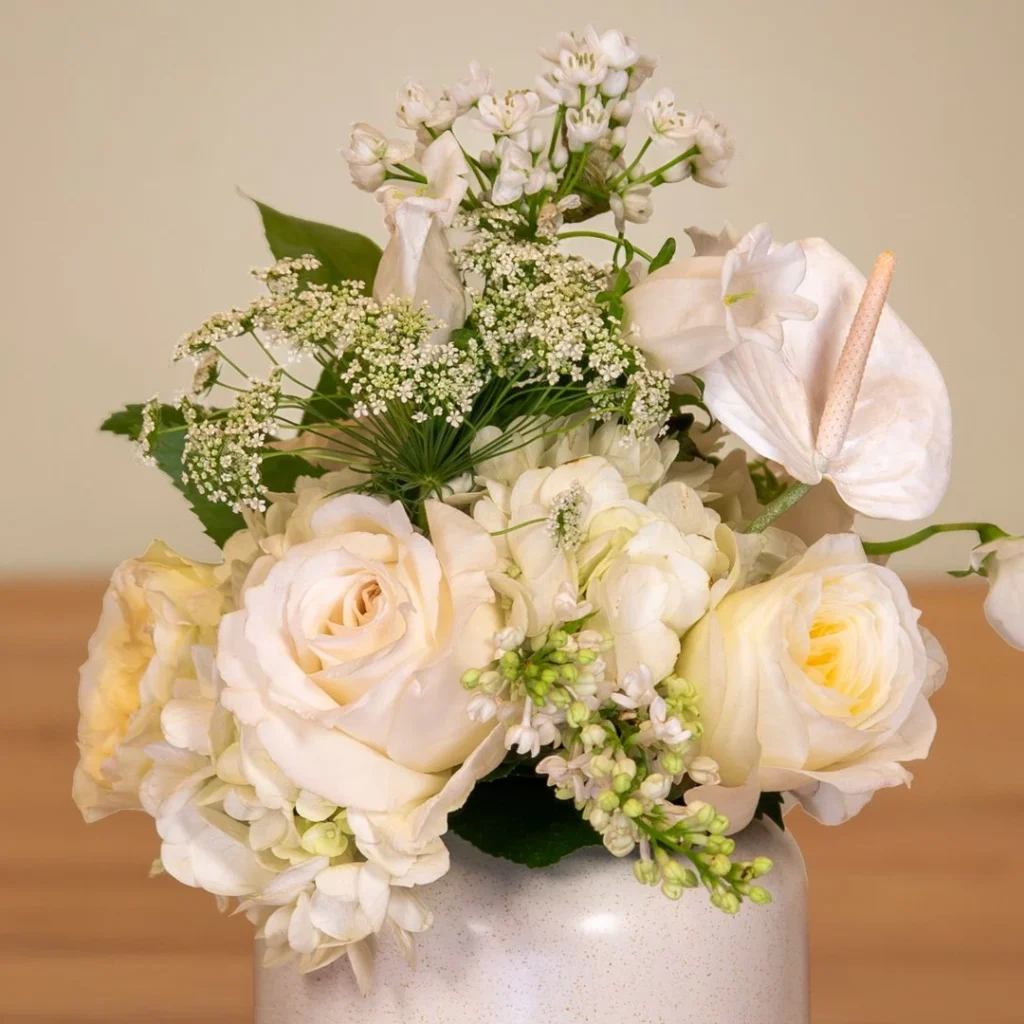 White floral arrangement inspired by Pantone Cloud Dancer featuring garden roses, hydrangea, Queen Anne’s lace, anthurium, and seasonal white blooms in a neutral ceramic vase
