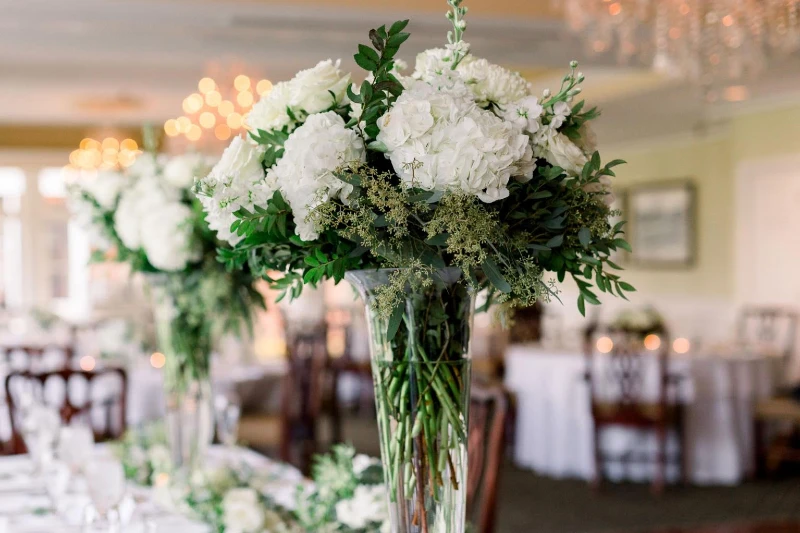 Tall green and white hydrangea centerpiece with greenery in glass vase at wedding reception